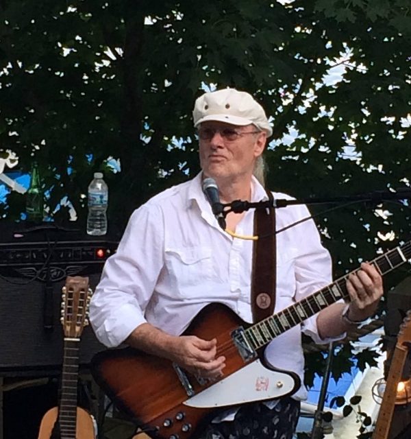 Allan Rhodes performing outside with a Gibson Firebird guitar.